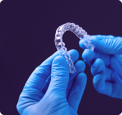 Mãos com luvas azuis segurando um alinhador dental transparente com fundo roxo, destacando detalhes do produto.