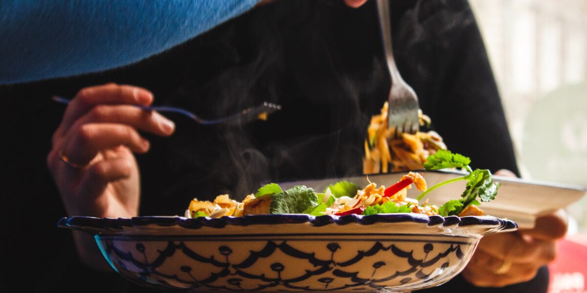 Pessoa com prato de comida e garfos na mão.