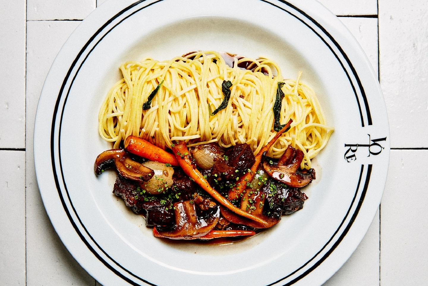 Prato de massa com macarrão, carne e legumes servidos em um prato branco.