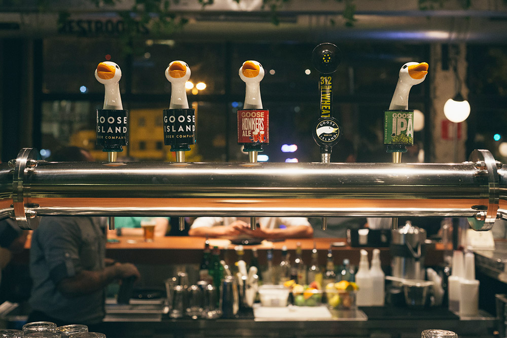 Torneiras de chope alinhadas em um bar, com rótulos de diferentes tipos de cerveja artesanal.