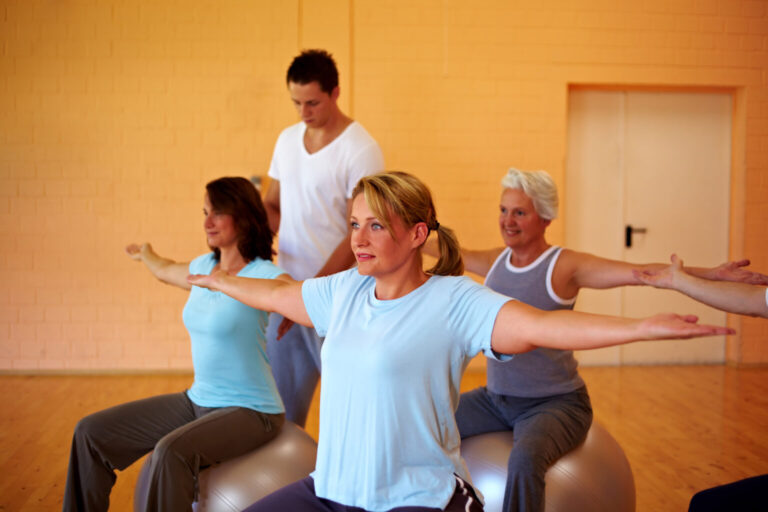 Várias mulheres fazendo aula com a bola de pilates e uma professora orientando